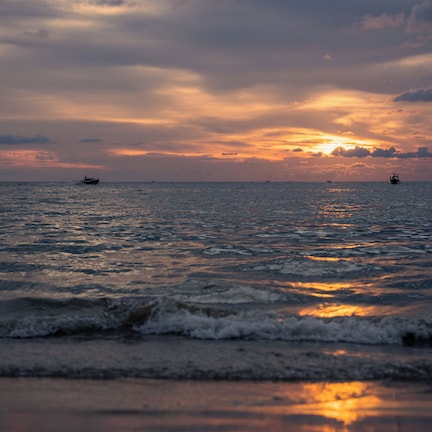 A sunset over a calm sea with boats and a distant ship.
