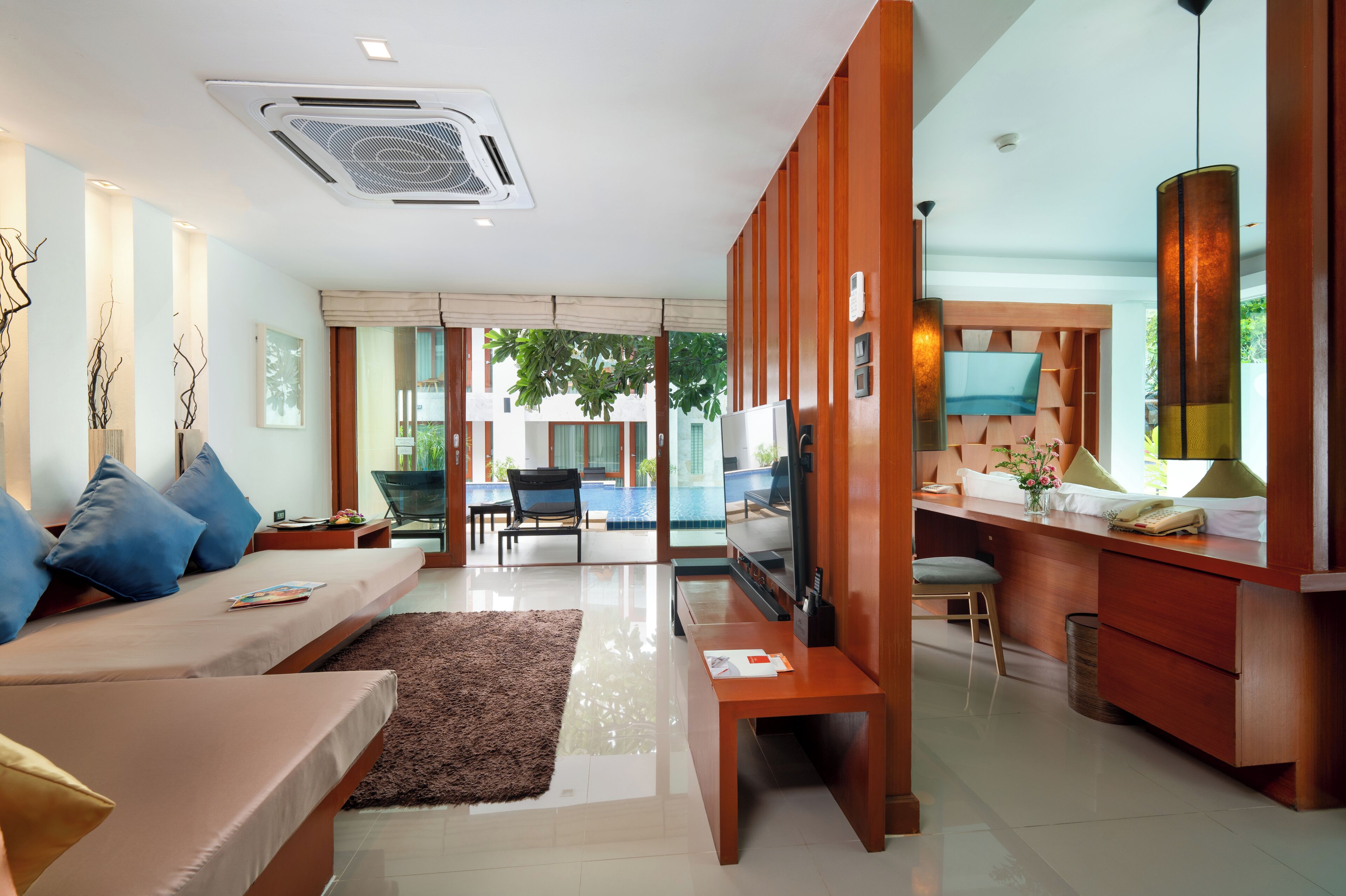 A modern living room with a sofa, a coffee table, and a TV. There is a dining area with a table and chairs, and a kitchen area with a counter and cabinets.