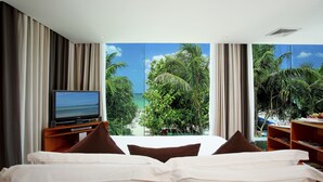 A hotel room with a bed, a TV, and a large window with a view of palm trees and the ocean. - La Flora Resort Patong (Patong)