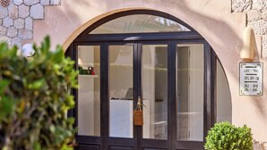 Une entrée d’immeuble avec une façade en pierre, une enseigne indiquant « Bien-être » et une plante en pot.