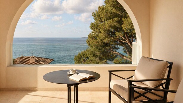 Un balcon avec vue sur la mer, une table avec un livre et une tasse, et une chaise.