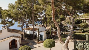 Une villa côtière à l’extérieur blanc, avec un chemin de pierre et un petit jardin agrémenté de cactus et d’un arbuste aux allures soignées.