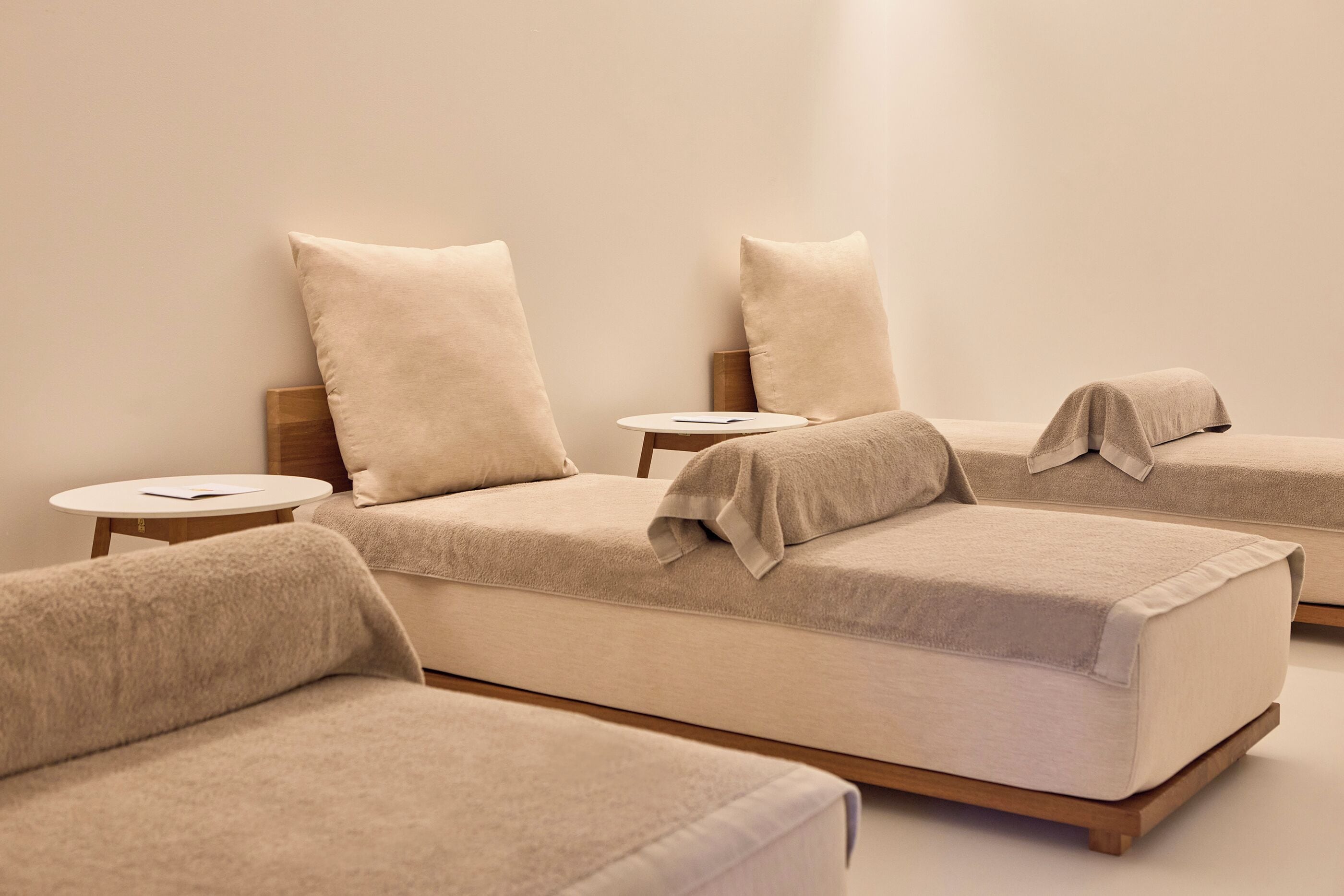 A minimalist room with three beds, each with a wooden headboard and a round side table.