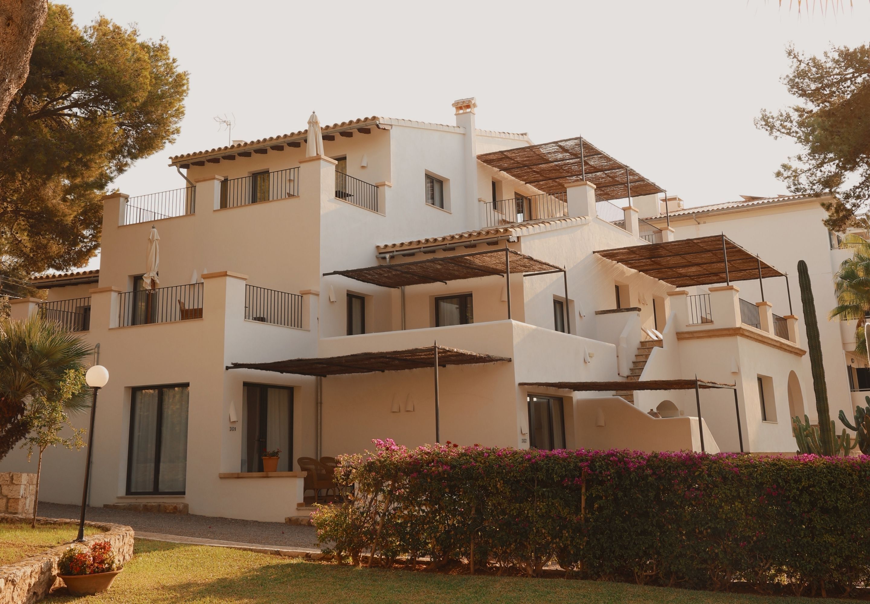 Un edificio residencial de varios pisos con balcones, un patio cubierto y un jardín bien cuidado.