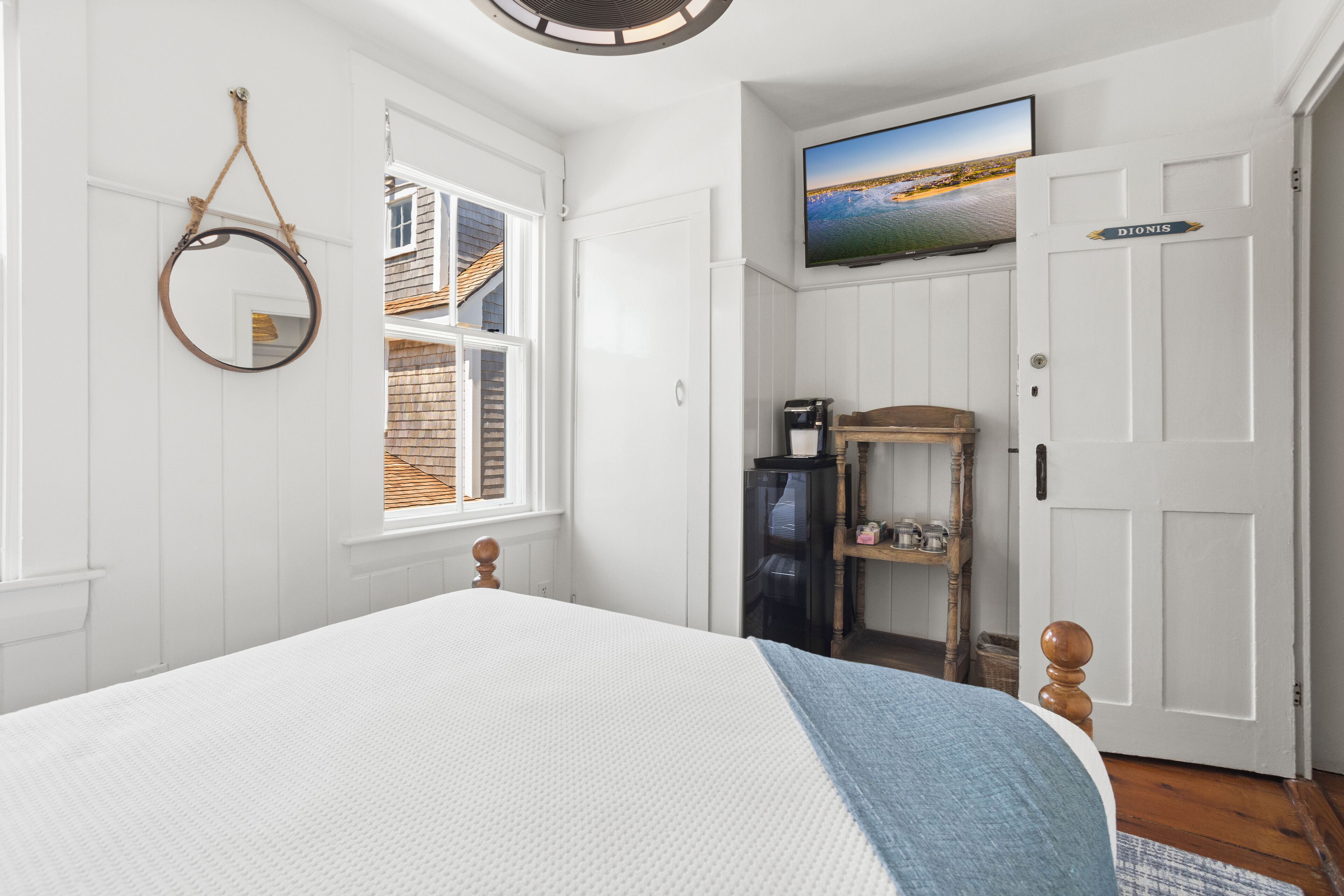 A bedroom with a bed, a television, a small shelf, and a door labeled "DIONIS".
