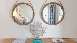 Two round mirrors with rope handles on a wall, a decorative metal tree sculpture, and a wooden table with magazines. - Carlisle House Inn (Nantucket)