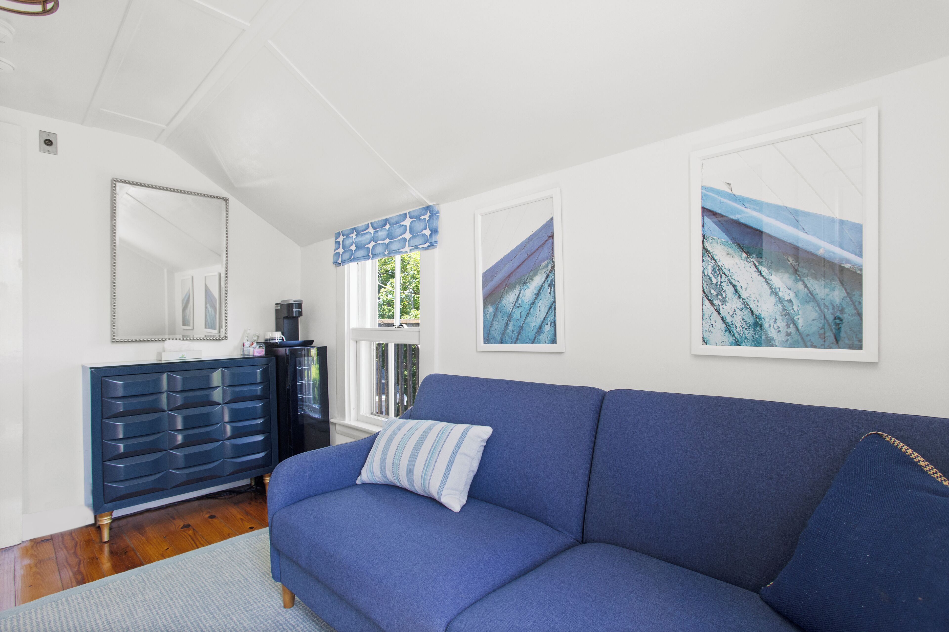A modern living room with a blue sofa, a dark blue dresser, and two framed artworks on the wall.