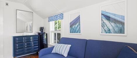 A modern living room with a blue sofa, a dark blue dresser, and two framed artworks on the wall.
