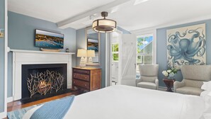 A bedroom with a fireplace, a bed, a chair, and artwork on the walls. - Carlisle House Inn (Nantucket)