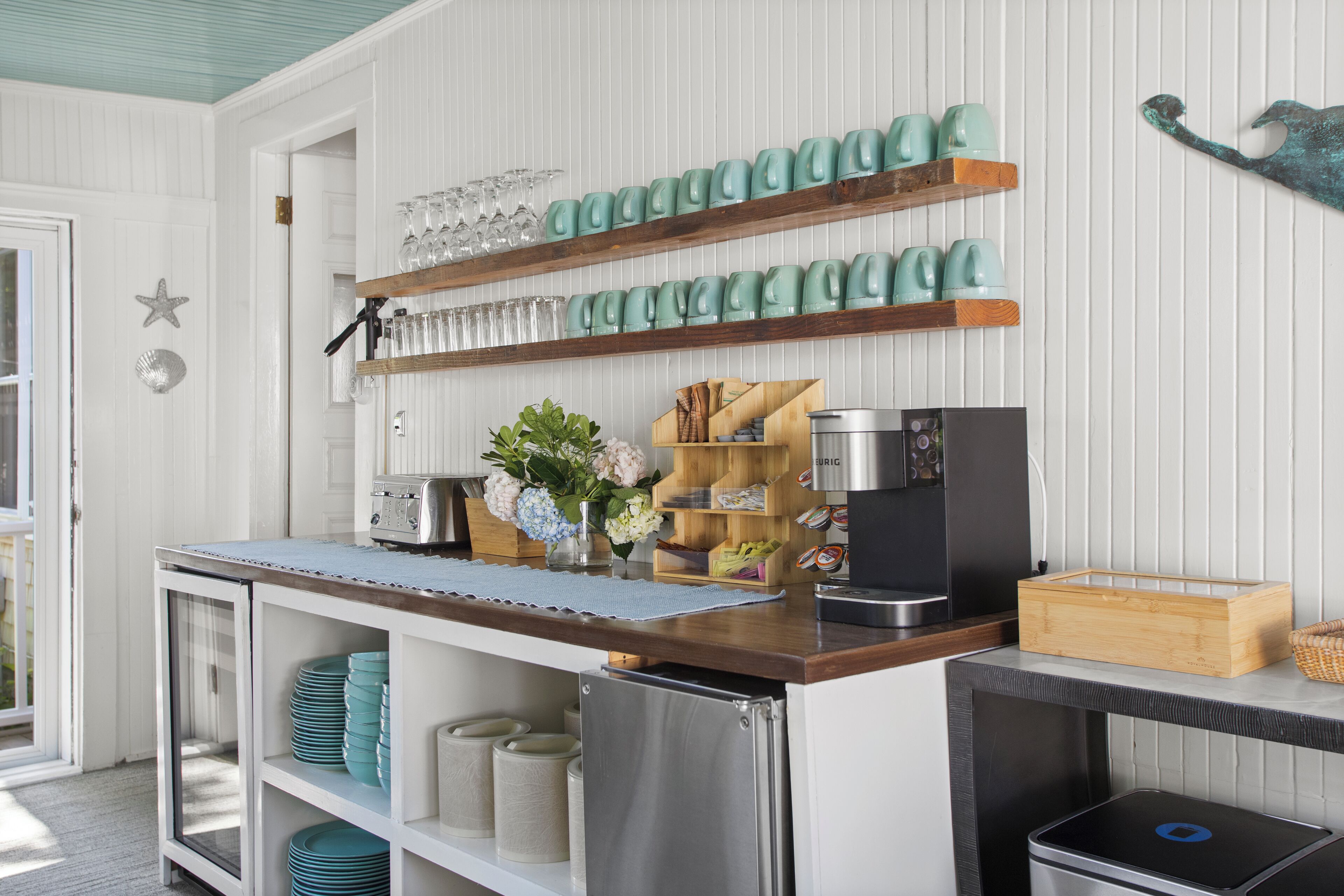 Een keuken met een houten aanrecht, roestvrijstalen apparatuur en teal-kleurige mokken op planken.