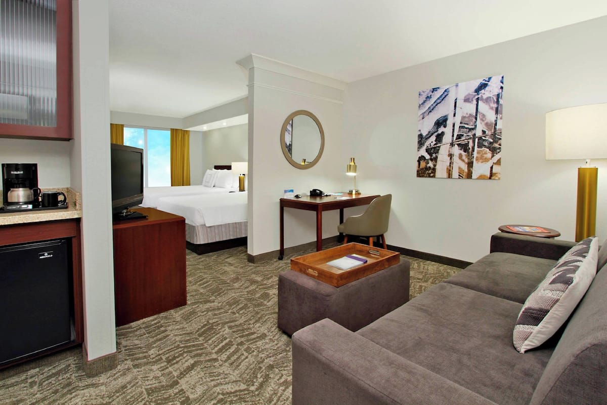 A hotel room with a bed, a desk, a television, a coffee maker, a small refrigerator, and a sofa.