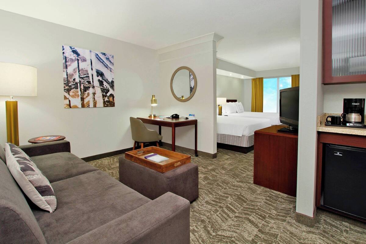 A hotel room with a sofa, a desk, a bed, a TV, and a coffee maker.