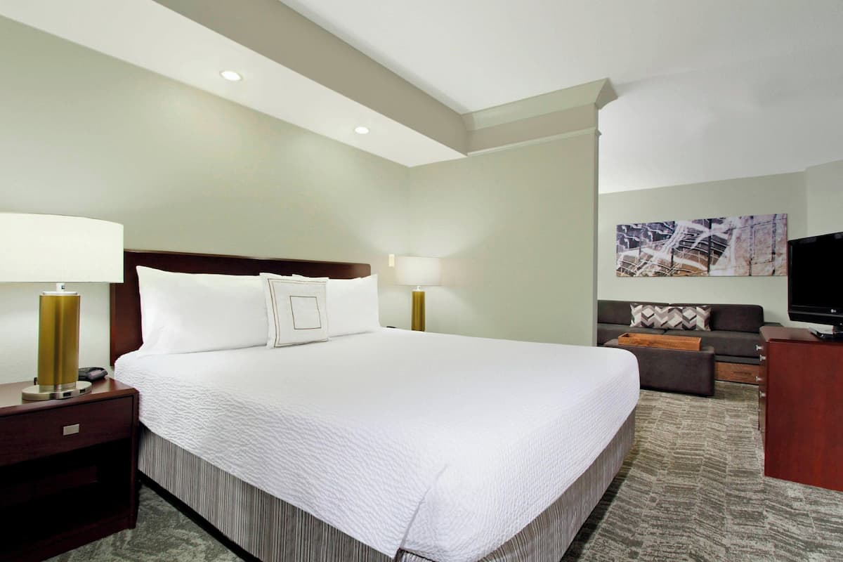 A hotel room with a large bed, two bedside tables with lamps, a sofa, a TV, and a painting on the wall.