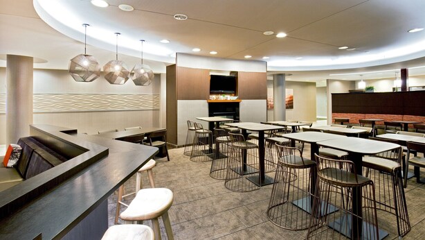 A modern restaurant with a central bar area, multiple seating options including high tables and bar stools, and a flat-screen TV mounted on a wooden panel. - SpringHill Suites by Marriott Chesapeake Greenbrier (Chesapeake)