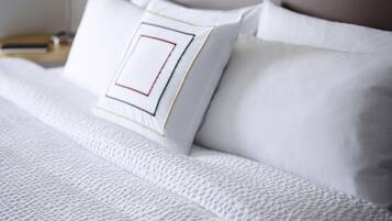 Una cama bien tendida con sábanas blancas y una almohada con un diseño geométrico.
