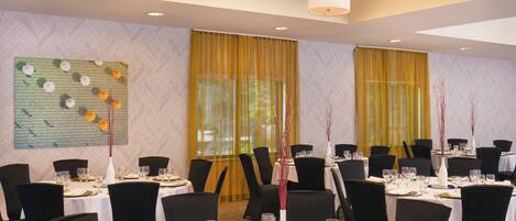 A dining area with round tables set for a meal, black chairs, and a large floral wall art piece.