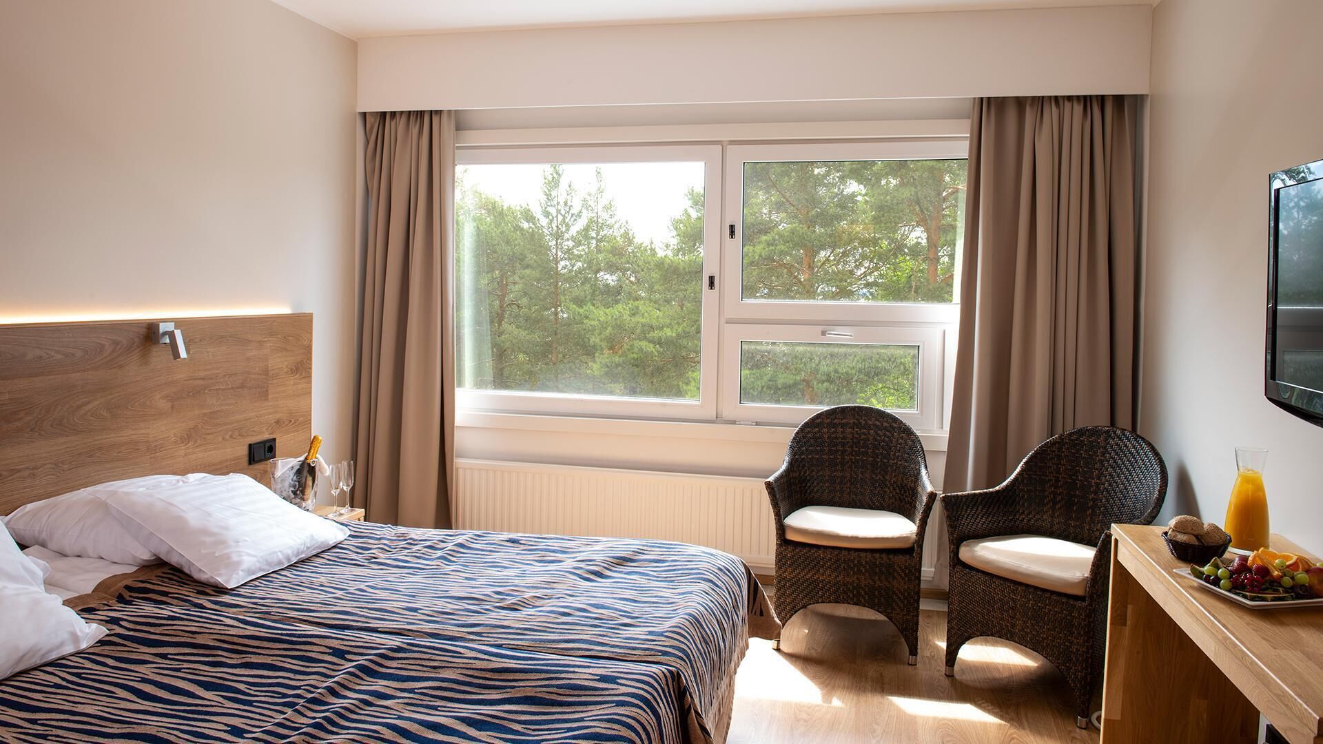 A hotel room with a bed, two chairs, a small table with fruit, and a TV.