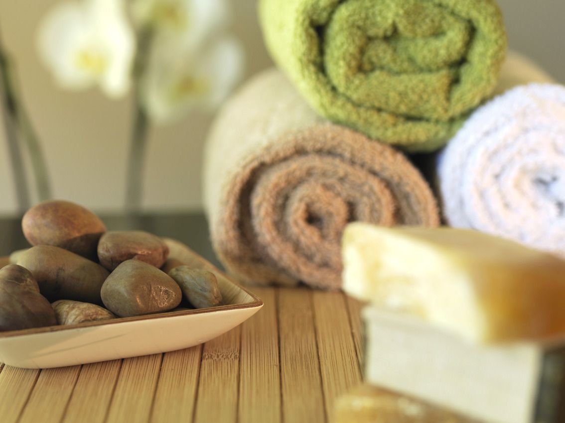 A wooden table with a bowl of smooth stones, rolled towels in various colors, and a bar of soap.