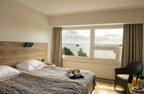 A hotel room with a bed, a chair, a table with breakfast items, and a large window with a view of the sea. - Ruissalo Spa Hotel (Turku)