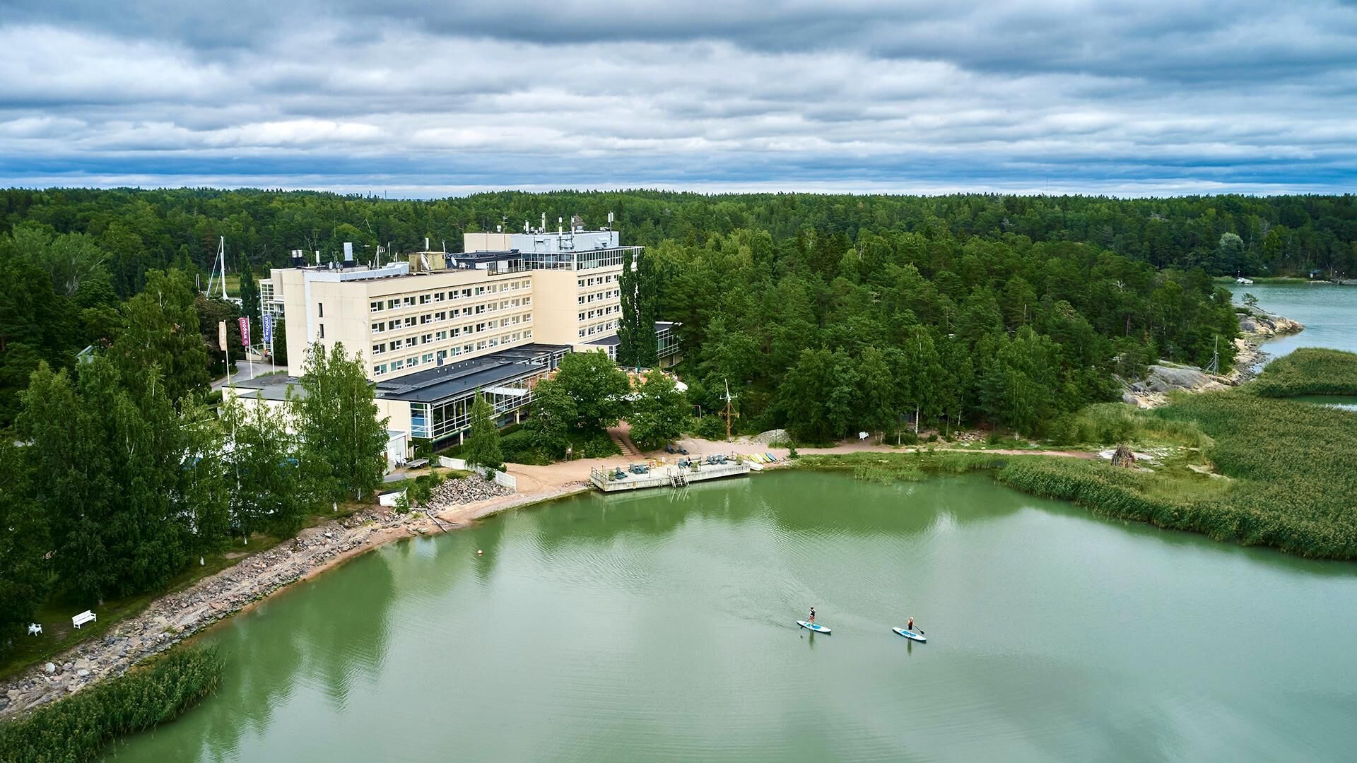 A hotel with a large building, a dock, and a lake surrounded by trees.