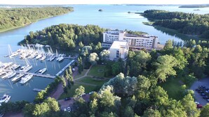A marina with multiple boats docked, surrounded by dense forest and a large building with a modern design. - Ruissalo Spa Hotel (Turku)