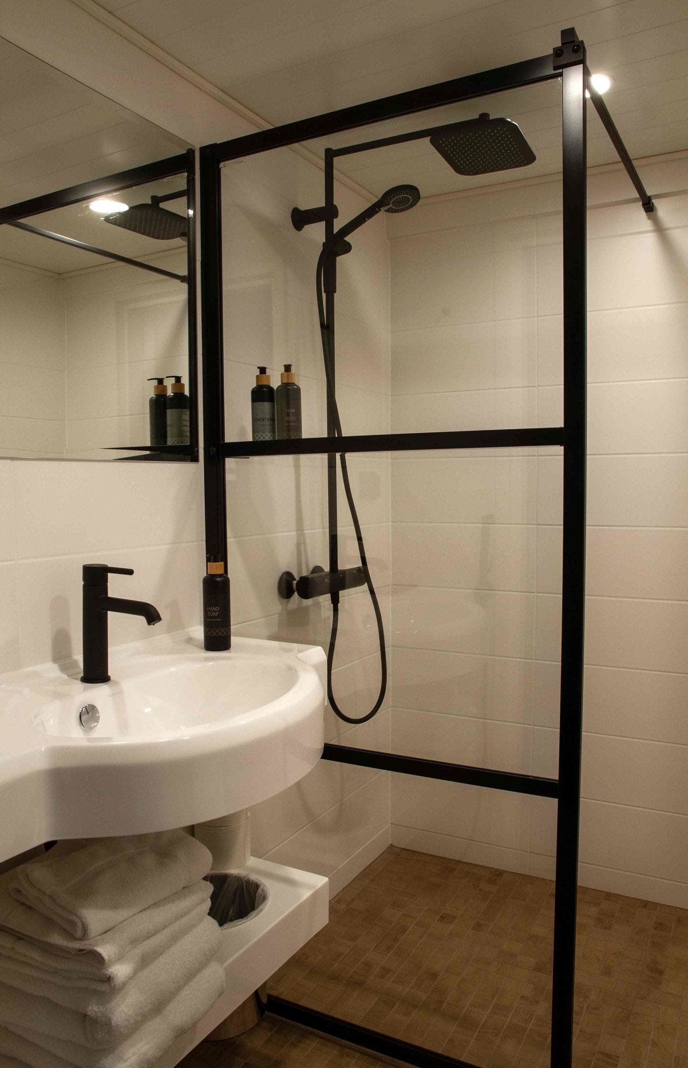 Ein Badezimmer mit einem weißen Waschbecken, einem schwarzen Wasserhahn und einer Duschkabine aus Glas.