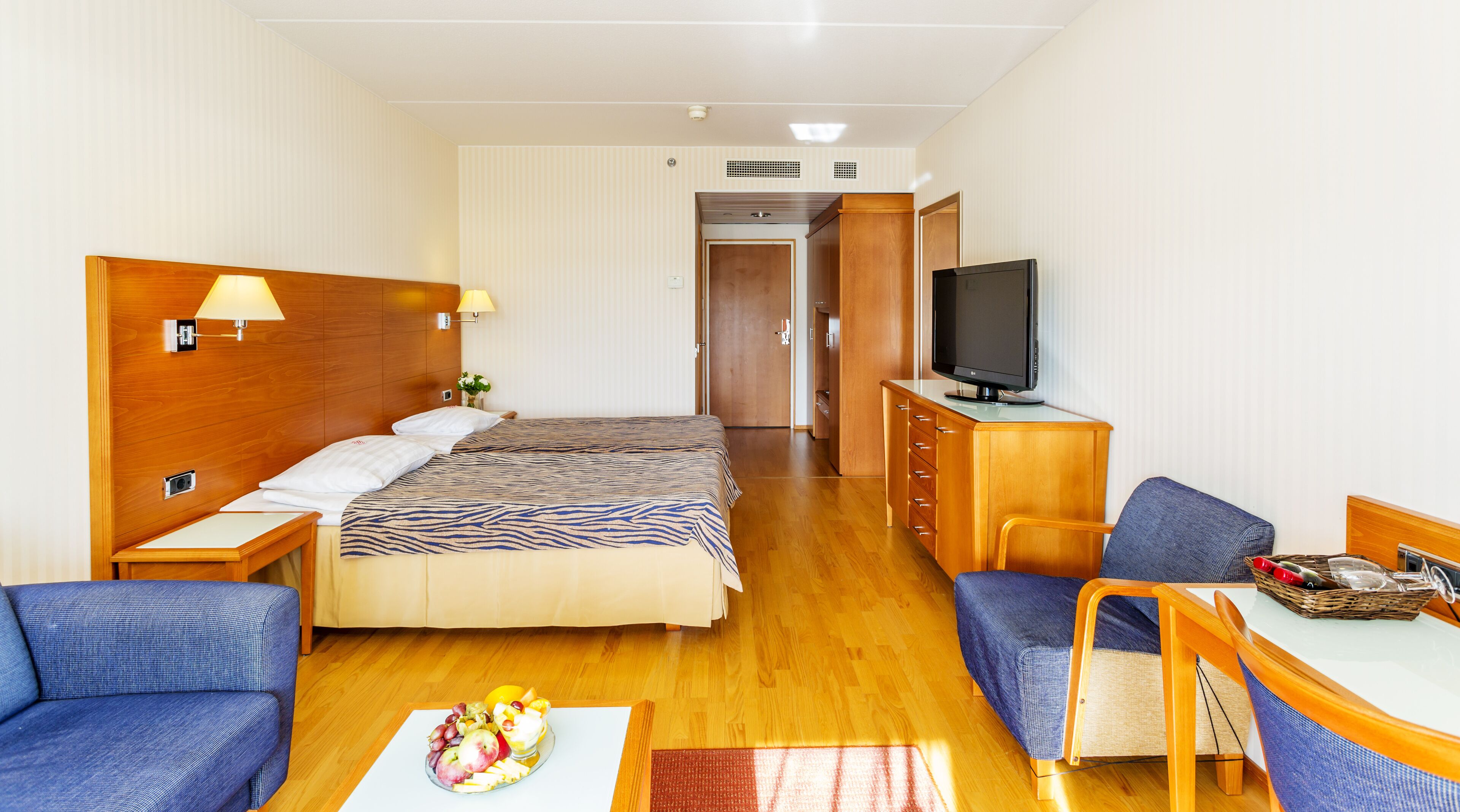 A hotel room with a bed, a TV, a desk, a chair, and a sofa.