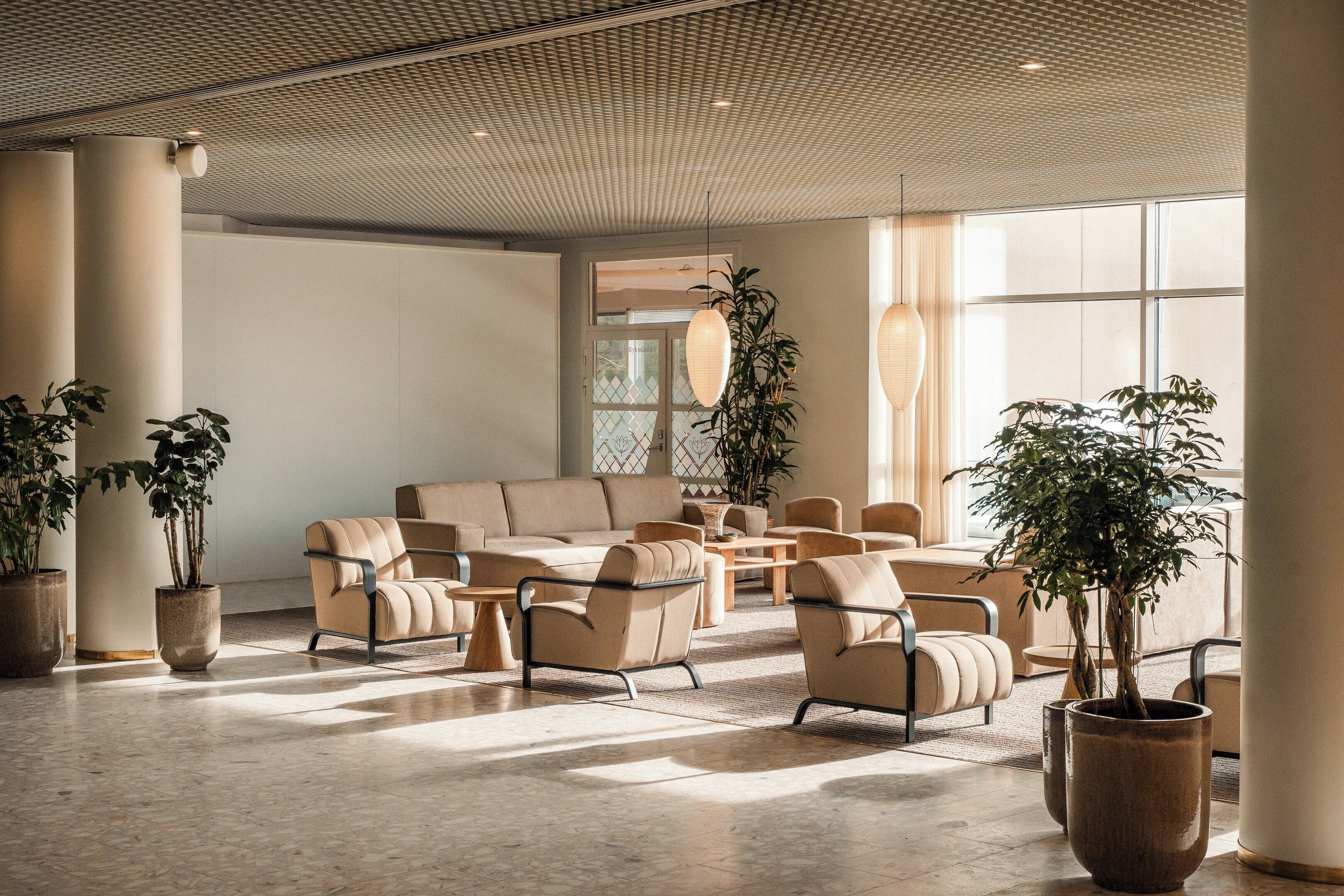 A spacious lobby with a modern design, featuring a large sofa, armchairs, and potted plants.