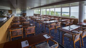 Ein Essbereich mit Tischen und Stühlen, großen Fenstern mit Blick auf das Wasser und einer Holzzieldecke.
