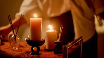 A candlelit table with a candle in a holder, a glass jar with a reed diffuser, and a small candle in a glass jar.