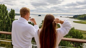 A couple standing on a balcony overlooking a river with trees and an island in the distance. - Ruissalo Spa Hotel (Turku)