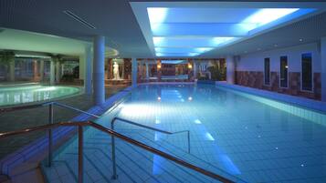 Una amplia piscina interior con suelo de baldosas, barandilla de vidrio y techo con tragaluces.