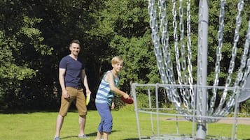 Two people playing frisbee in a park with a metal disc golf basket.