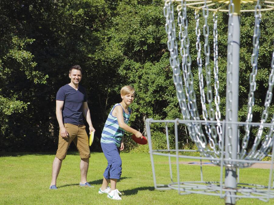 Two people playing frisbee in a park with a metal disc golf basket.