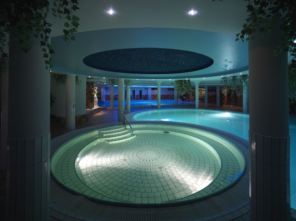 A circular indoor pool with a starry ceiling, surrounded by columns and plants.