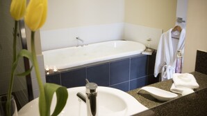 A bathroom with a bathtub, a sink, and a mirror. There are towels and a robe hanging on the wall.