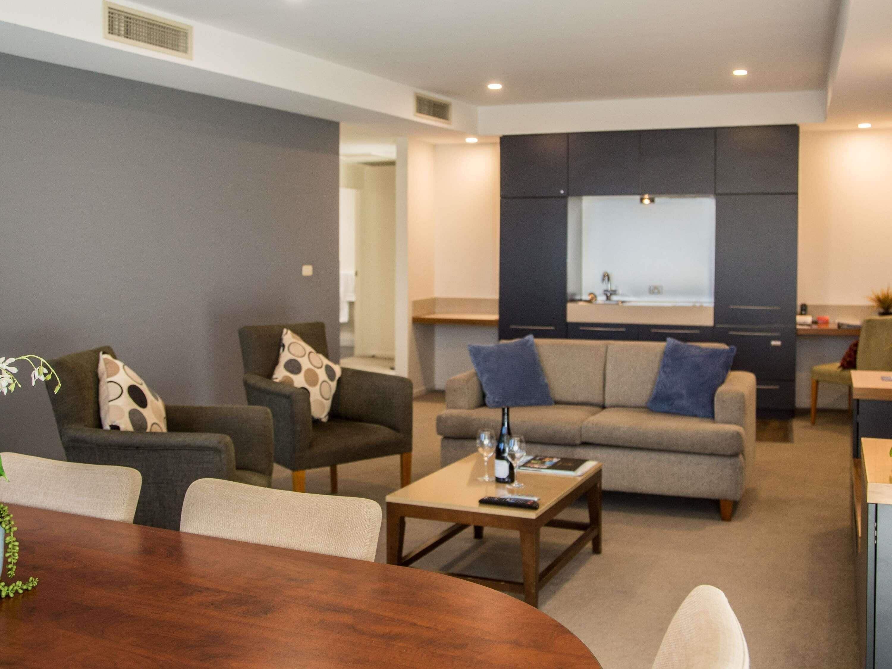 A modern living room with a dining table, sofas, and a kitchen area in the background.