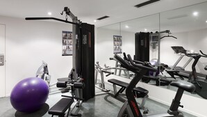 A gym with exercise equipment, a large mirror, and a purple exercise ball.