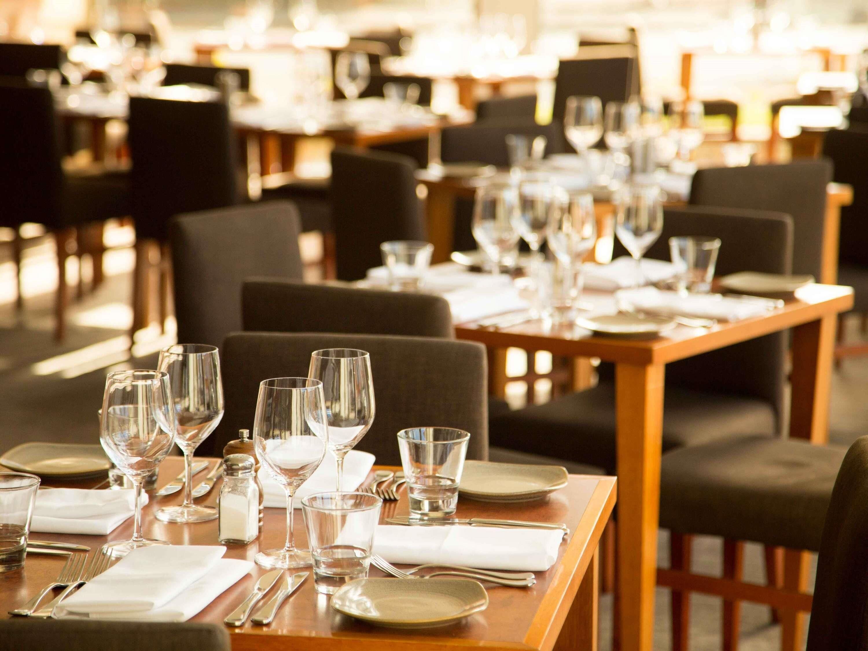 Un restaurante con mesas dispuestas para comer, incluyendo copas de vino, vasos de agua y cubiertos.