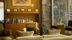A library with bookshelves, a framed painting, and a stone wall. - The Sebel Launceston (Launceston)