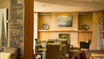 A lobby with stone walls, a fireplace, and several armchairs.