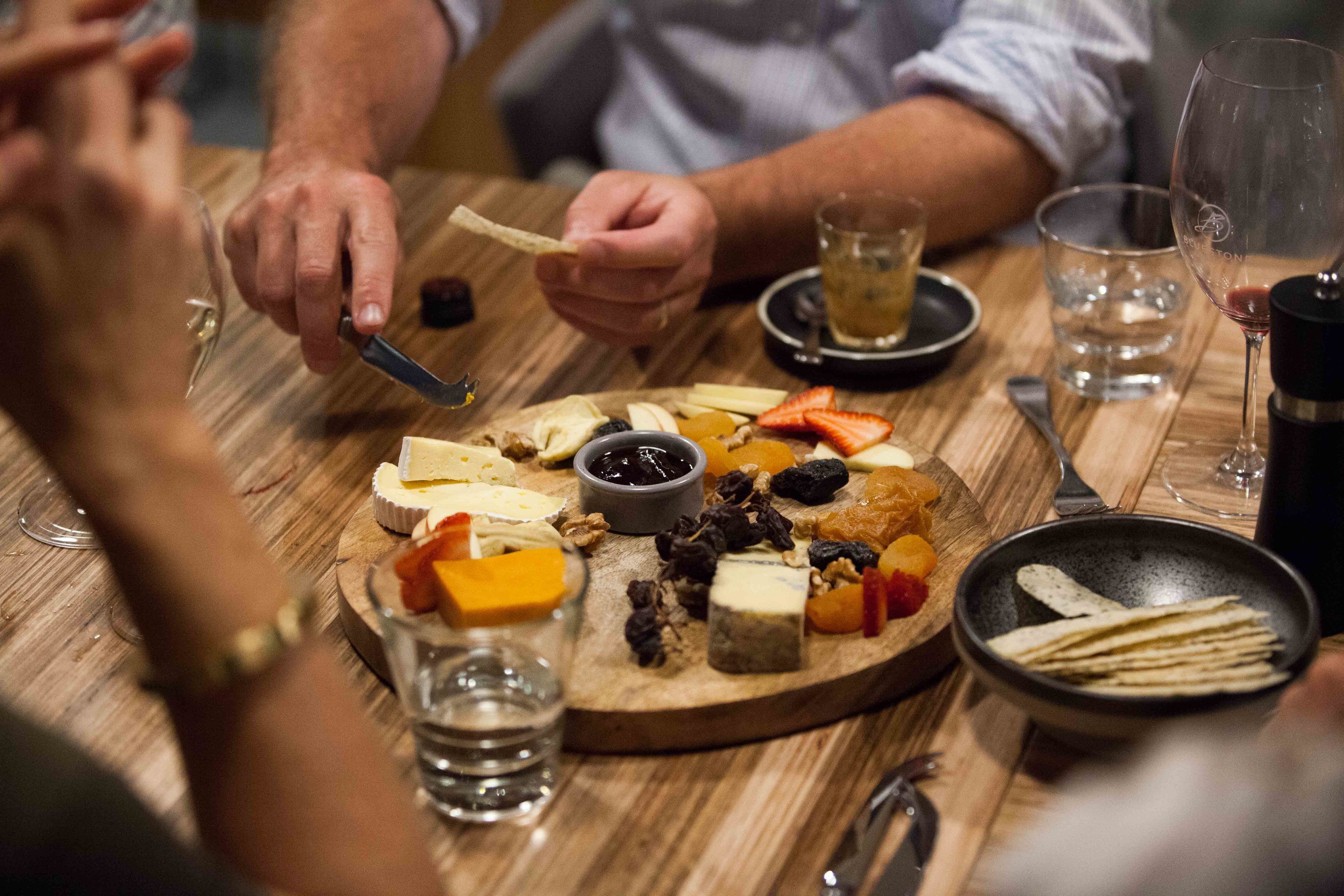 A wooden board with various cheeses, fruits, and nuts.