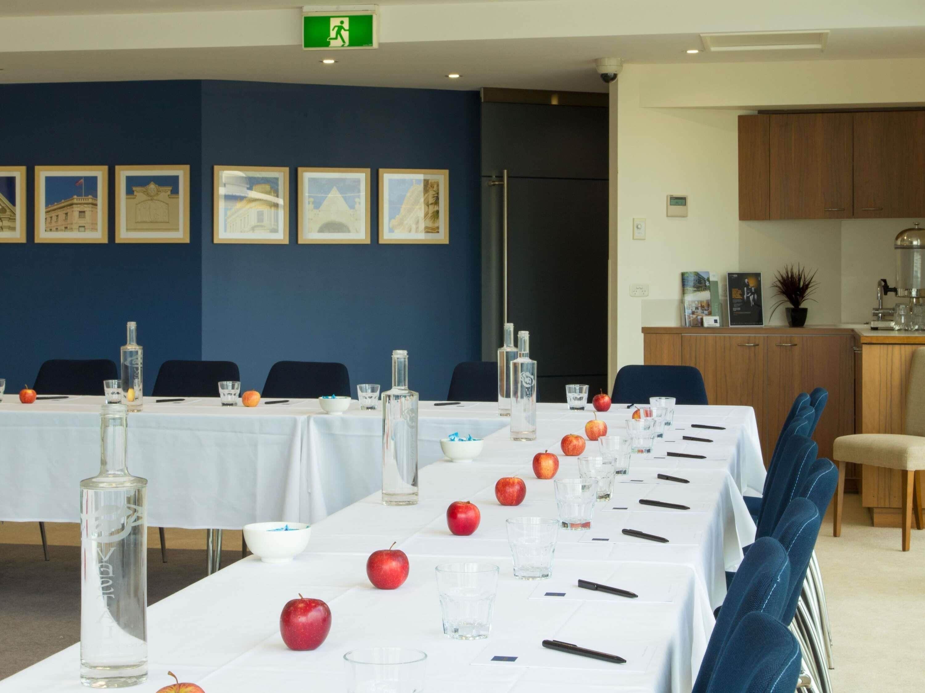 A conference room with tables set for meetings, framed pictures on the wall, and a kitchenette area.