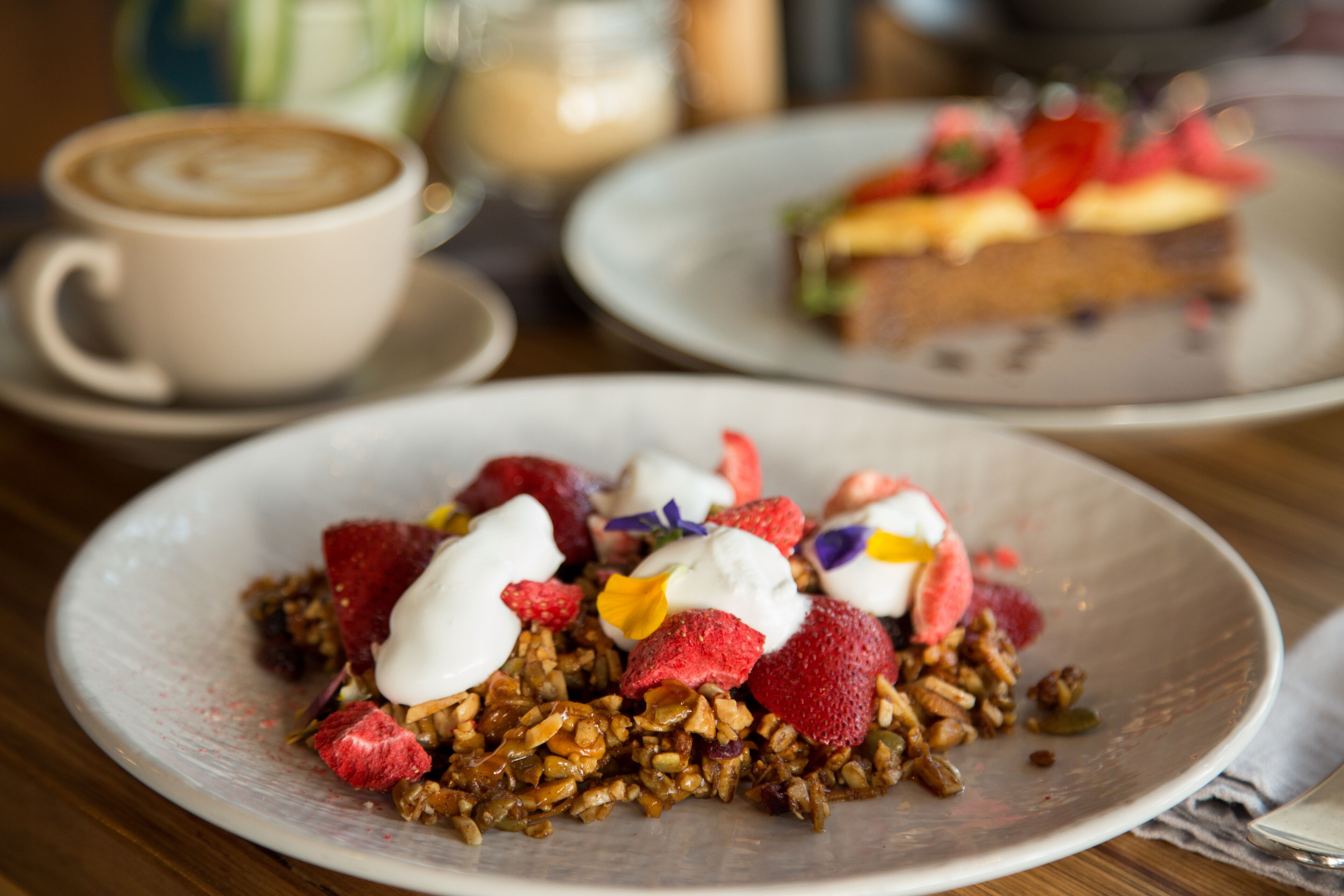 Un plato de postre con granola, fresas y crema batida.