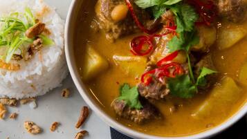 Uma tigela de curry com carne e vegetais, decorada com pimenta vermelha e coentro, acompanhada de arroz branco.