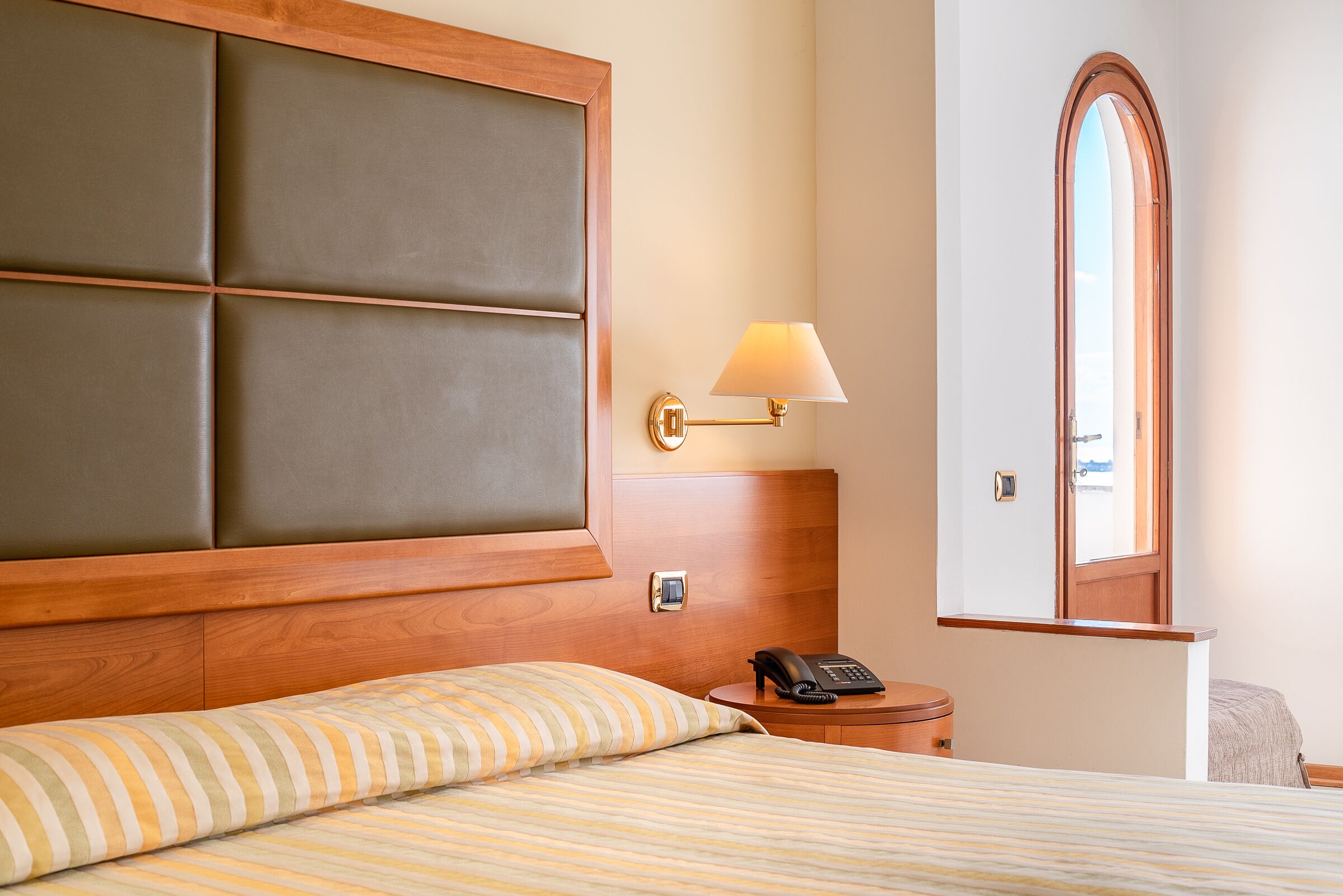 A hotel room with a large bed, a bedside telephone, a nightstand, and a lamp.