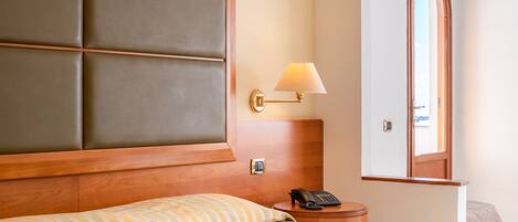 A hotel room with a large bed, a bedside telephone, a nightstand, and a lamp.