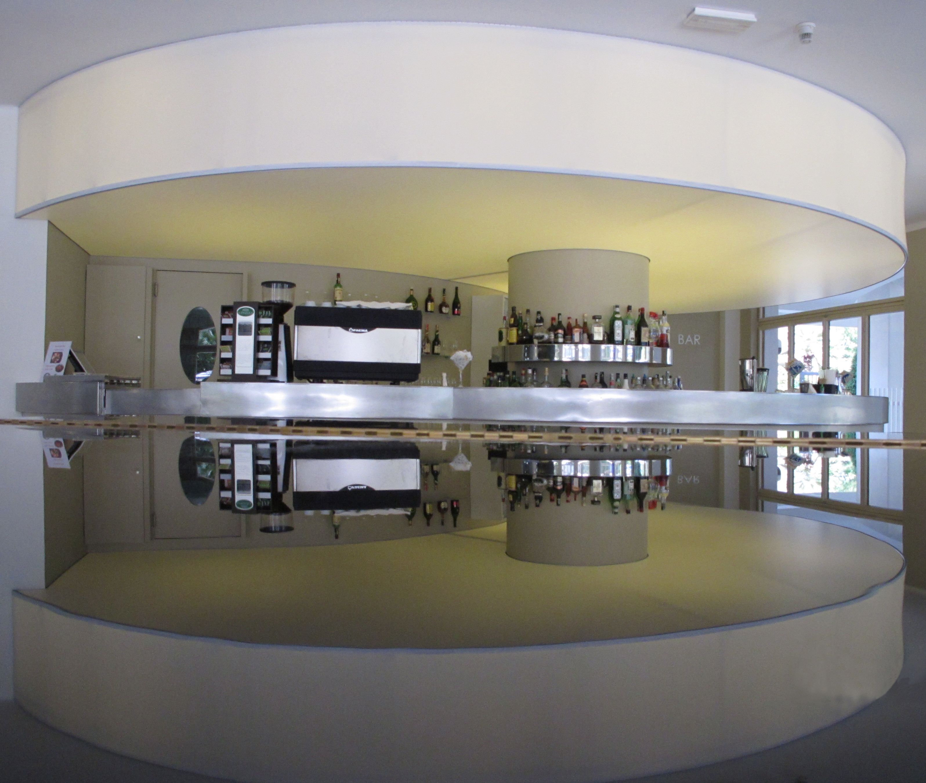 A modern bar with a reflective floor, a central bar counter, and shelves of bottles.