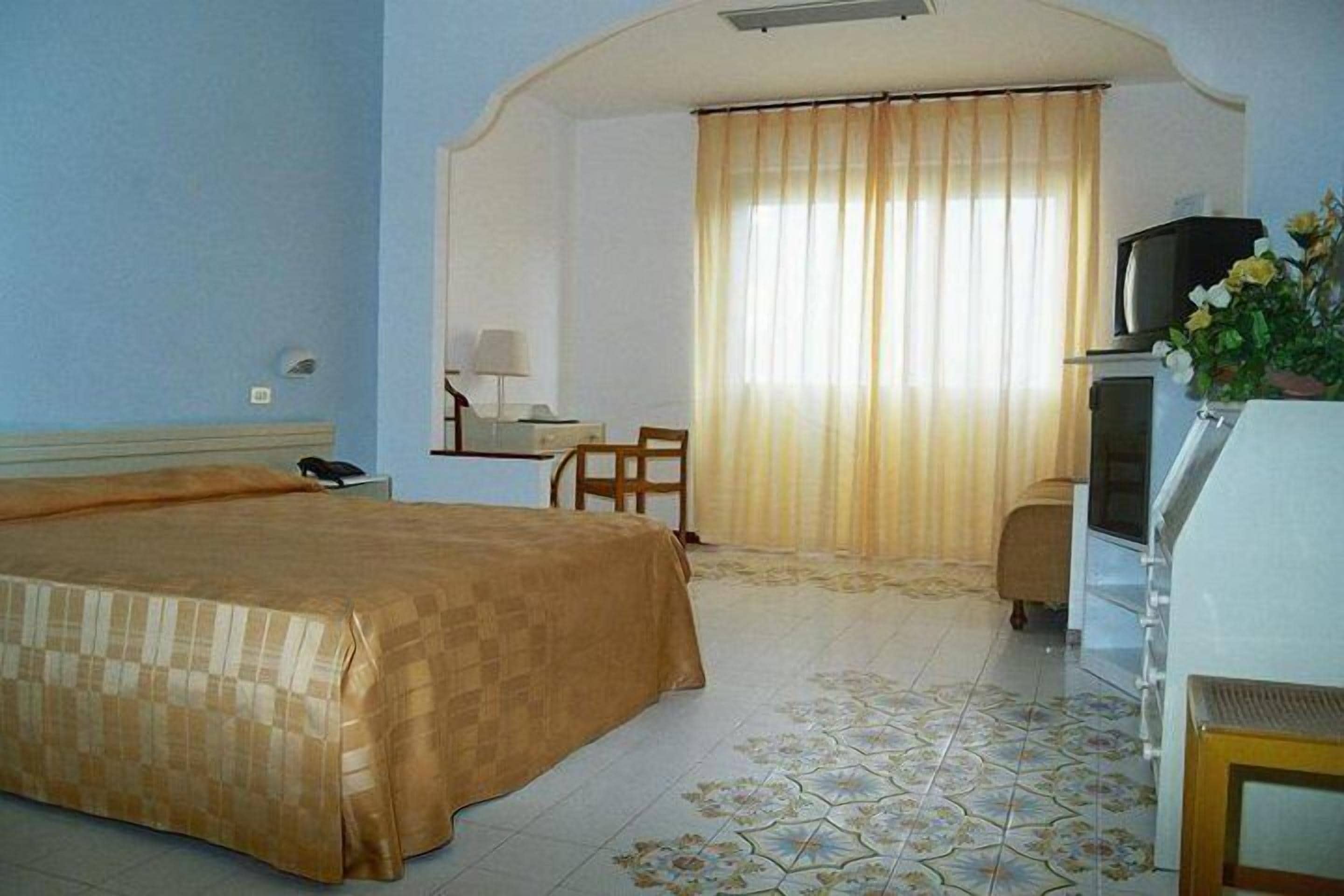 A hotel room with a bed, a desk, a chair, a television, and a window with curtains.