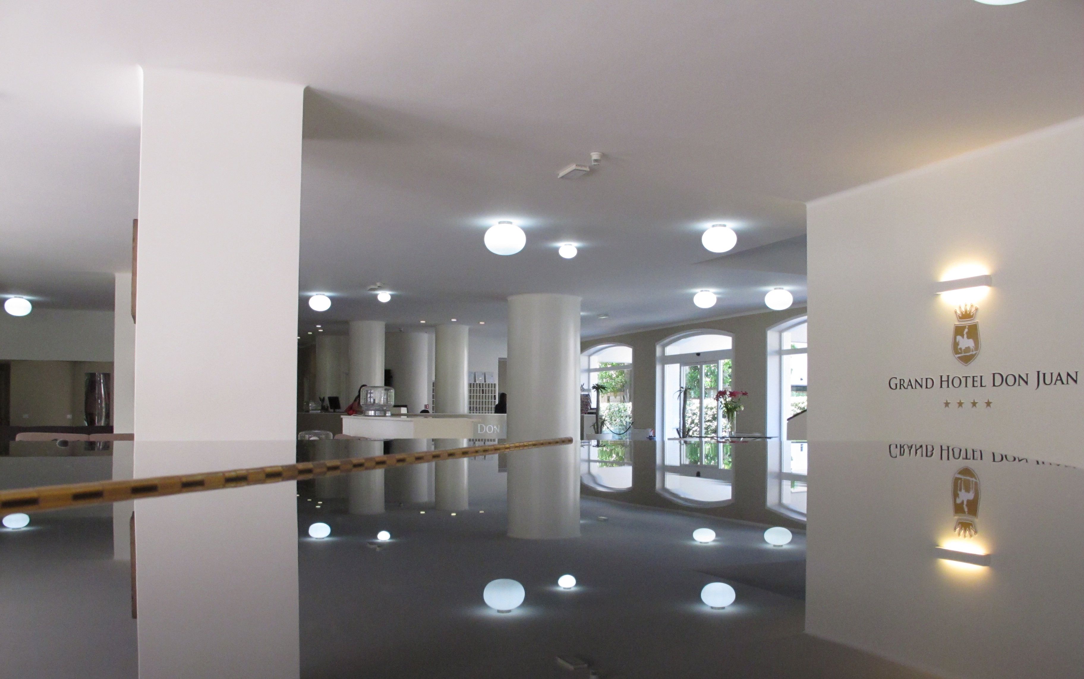 A modern hotel lobby with a reflective floor, large pillars, and a reception desk.
